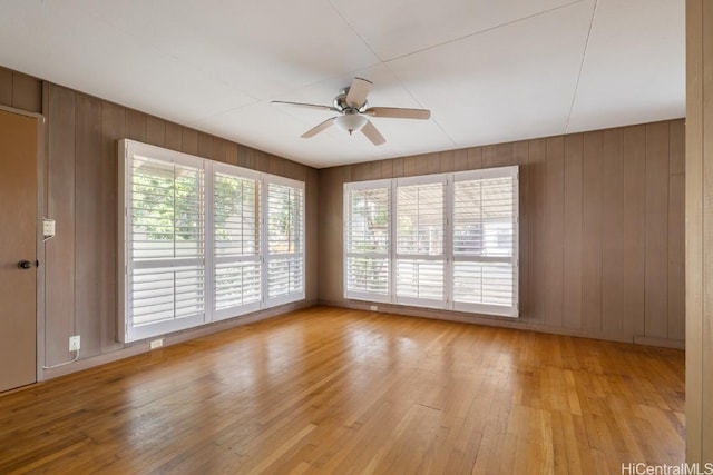 empty room with wooden walls, light hardwood / wood-style floors, and ceiling fan