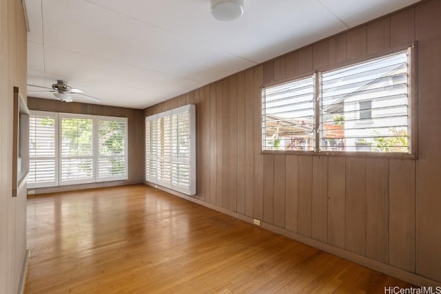 unfurnished room with ceiling fan, wooden walls, a wealth of natural light, and light wood-type flooring