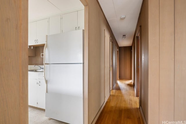 corridor with sink, wooden walls, and light wood-type flooring