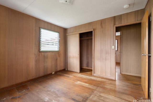 unfurnished bedroom with wood walls, a closet, and light wood-type flooring