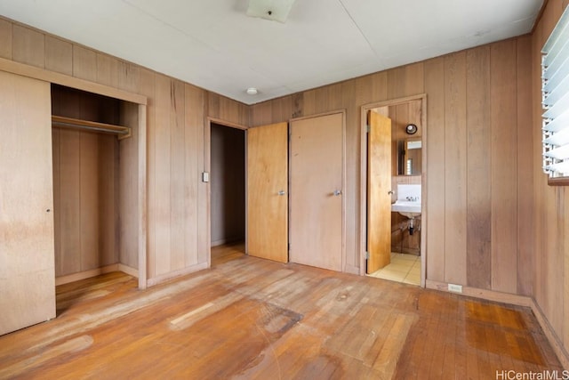 unfurnished bedroom with connected bathroom, wooden walls, and light wood-type flooring