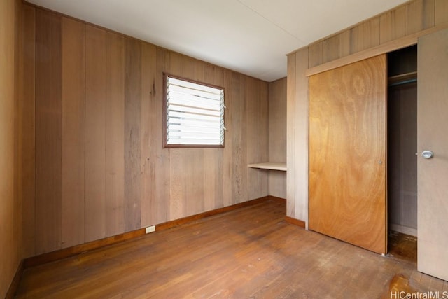 unfurnished bedroom featuring wood-type flooring, wooden walls, and a closet