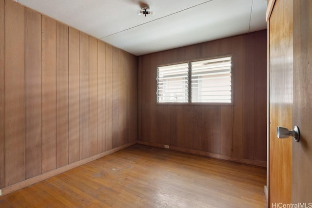 spare room with light wood-type flooring and wood walls