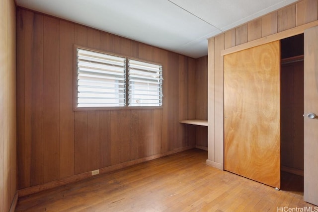 unfurnished bedroom with wooden walls, light hardwood / wood-style floors, and a closet