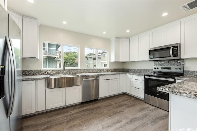 kitchen with appliances with stainless steel finishes, stone countertops, wood-type flooring, sink, and white cabinets