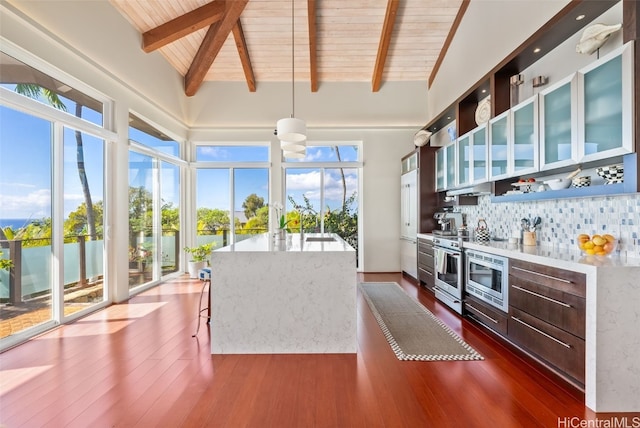 kitchen featuring tasteful backsplash, decorative light fixtures, high vaulted ceiling, dark hardwood / wood-style floors, and a kitchen island with sink