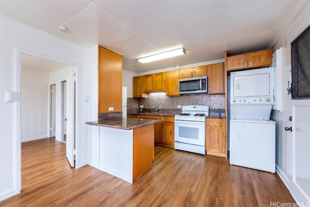 kitchen with white range with gas stovetop, hardwood / wood-style floors, stacked washer / dryer, decorative backsplash, and kitchen peninsula