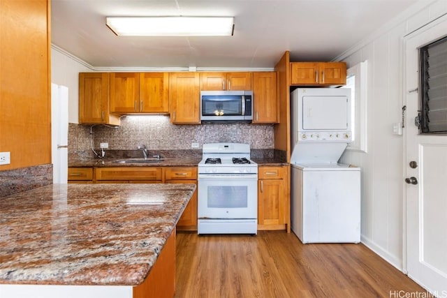 kitchen featuring sink, white range with gas stovetop, stacked washer / dryer, light hardwood / wood-style floors, and stone countertops