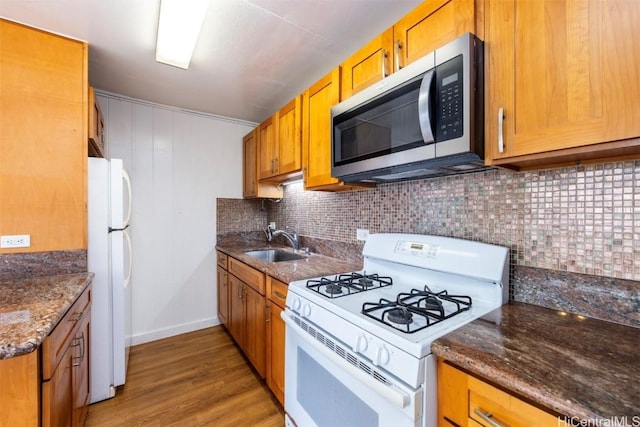 kitchen with sink, white appliances, backsplash, light hardwood / wood-style floors, and dark stone counters