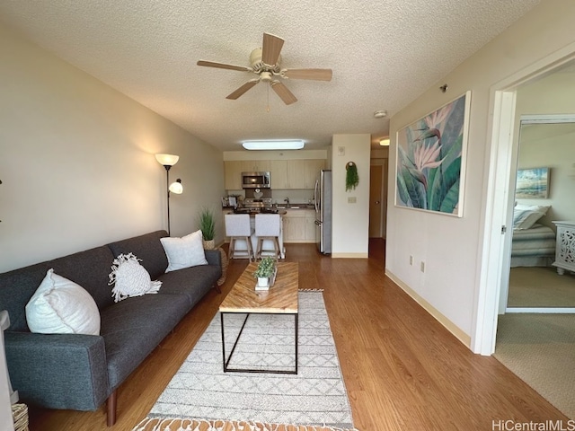 living room featuring ceiling fan, a textured ceiling, and light wood-type flooring