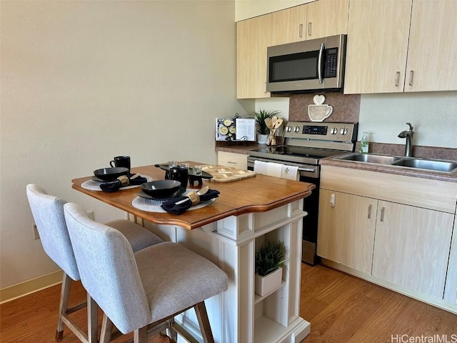 kitchen featuring sink, a kitchen bar, stainless steel appliances, light brown cabinets, and light hardwood / wood-style flooring