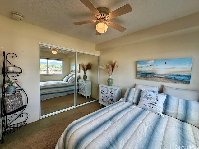 bedroom featuring ceiling fan, a textured ceiling, dark carpet, and a closet