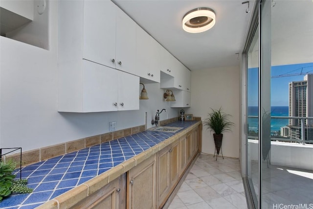 kitchen featuring white cabinetry, sink, tile countertops, and a water view