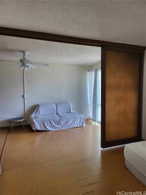 unfurnished bedroom featuring ceiling fan, a textured ceiling, wood-type flooring, and beamed ceiling