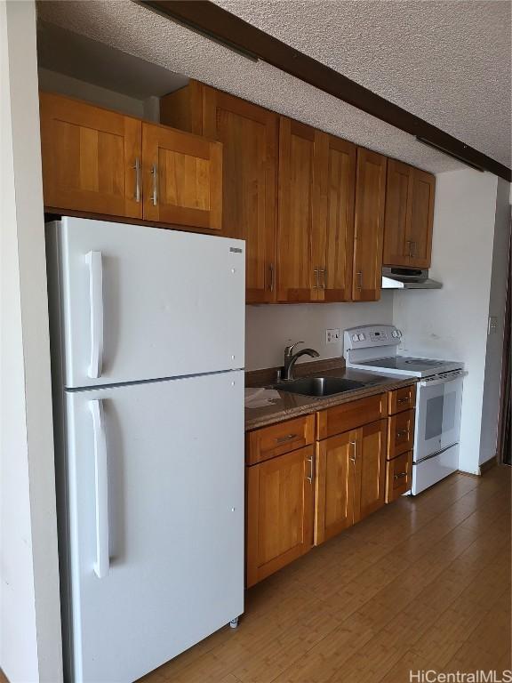 kitchen featuring sink, white appliances, beam ceiling, wood-type flooring, and a textured ceiling