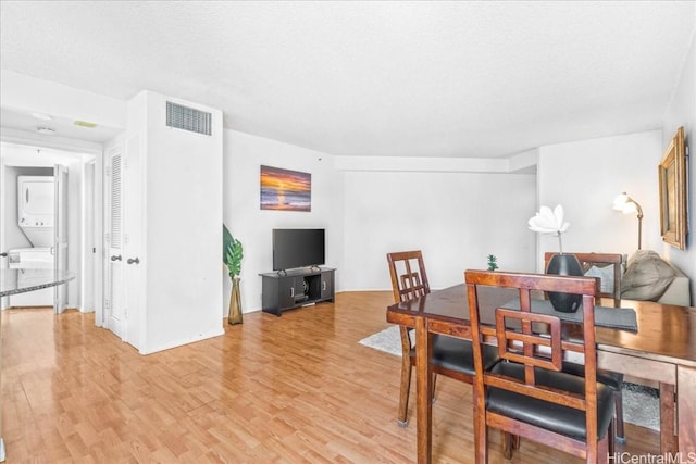 dining space with stacked washer / drying machine and light hardwood / wood-style floors