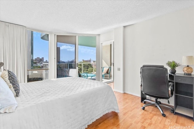 bedroom featuring access to exterior, hardwood / wood-style flooring, expansive windows, and a textured ceiling