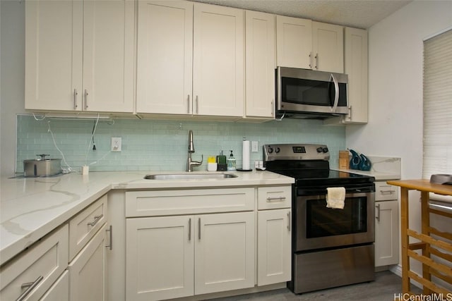 kitchen with light stone countertops, appliances with stainless steel finishes, sink, and white cabinets