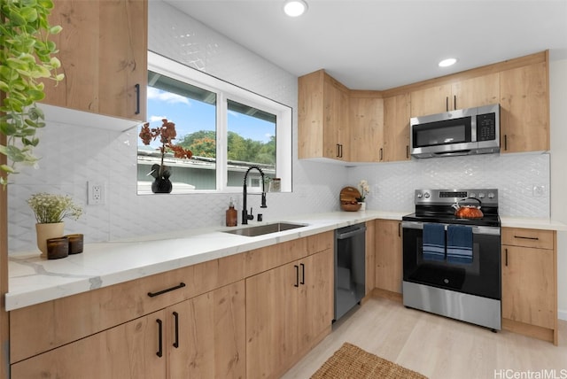 kitchen featuring sink, appliances with stainless steel finishes, light hardwood / wood-style floors, light stone countertops, and light brown cabinets