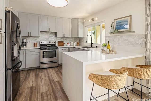 kitchen featuring sink, hardwood / wood-style flooring, appliances with stainless steel finishes, a kitchen breakfast bar, and kitchen peninsula