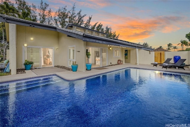 back house at dusk with a fenced in pool and a patio area