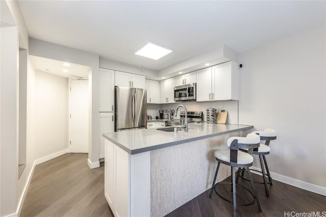 kitchen with sink, stainless steel appliances, white cabinets, a kitchen bar, and kitchen peninsula