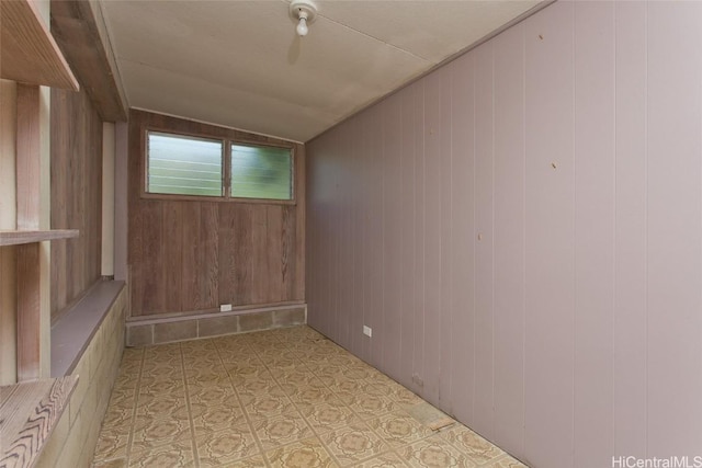 empty room featuring vaulted ceiling and wood walls