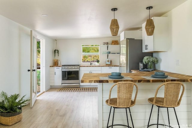 kitchen with pendant lighting, a breakfast bar area, wooden counters, appliances with stainless steel finishes, and white cabinets