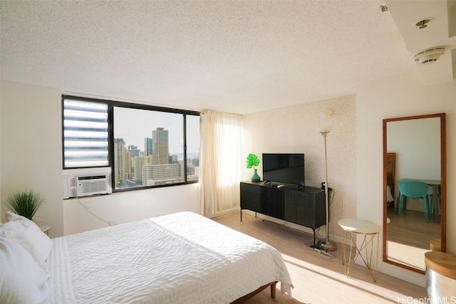 bedroom with cooling unit, a textured ceiling, and light hardwood / wood-style flooring