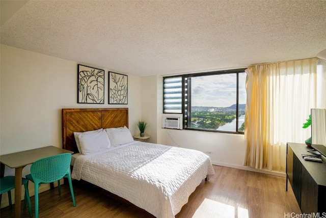 bedroom featuring cooling unit, light hardwood / wood-style flooring, and a textured ceiling