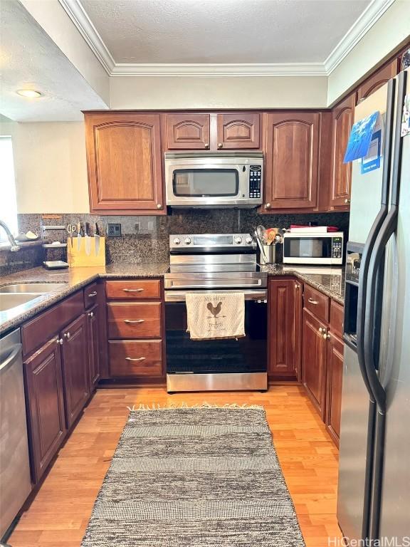 kitchen with ornamental molding, appliances with stainless steel finishes, sink, and light hardwood / wood-style flooring