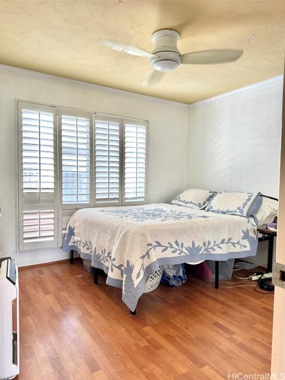 bedroom featuring multiple windows, wood-type flooring, ornamental molding, and ceiling fan