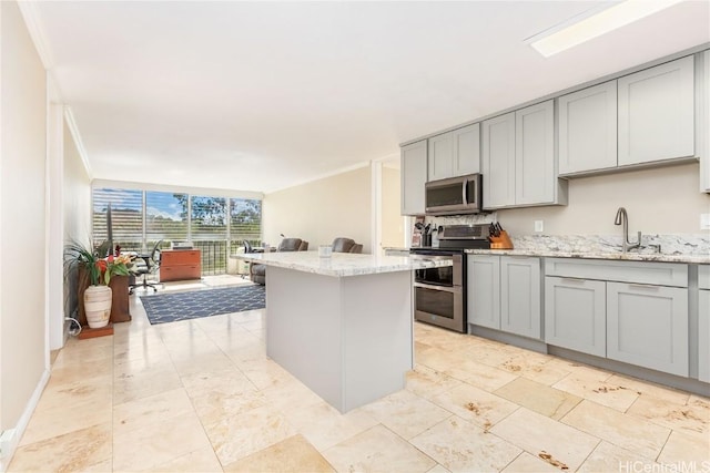 kitchen with gray cabinetry, light stone countertops, stainless steel appliances, and sink