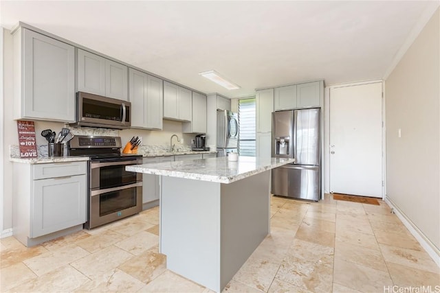 kitchen with a kitchen island, light stone countertops, appliances with stainless steel finishes, and gray cabinetry