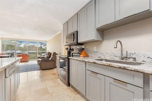 kitchen featuring sink, gray cabinetry, light stone counters, ornamental molding, and appliances with stainless steel finishes