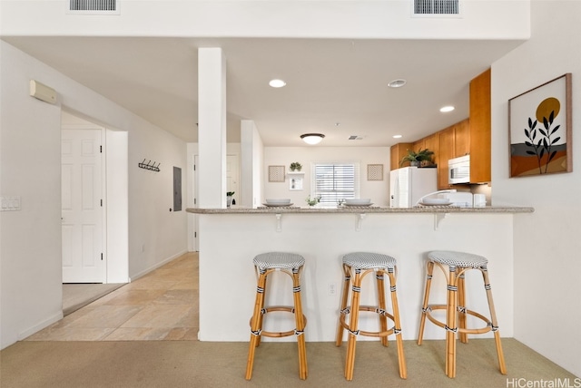 kitchen with light stone counters, a breakfast bar, kitchen peninsula, and white fridge