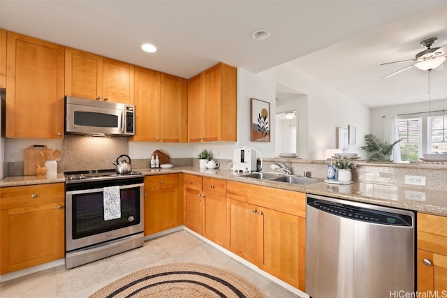 kitchen with light stone countertops, appliances with stainless steel finishes, sink, and ceiling fan