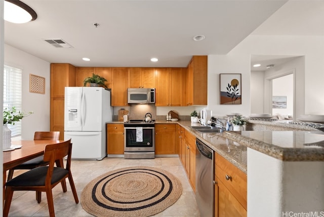 kitchen featuring sink, light tile patterned floors, stainless steel appliances, light stone counters, and kitchen peninsula