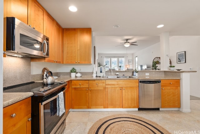 kitchen with sink, light stone counters, kitchen peninsula, ceiling fan, and stainless steel appliances