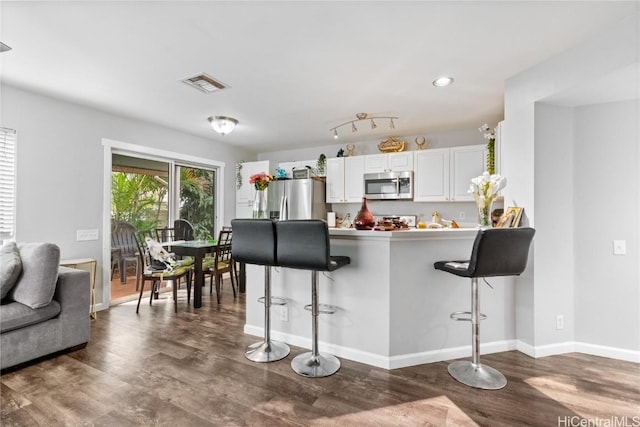 kitchen featuring white cabinetry, appliances with stainless steel finishes, dark hardwood / wood-style flooring, a kitchen breakfast bar, and kitchen peninsula