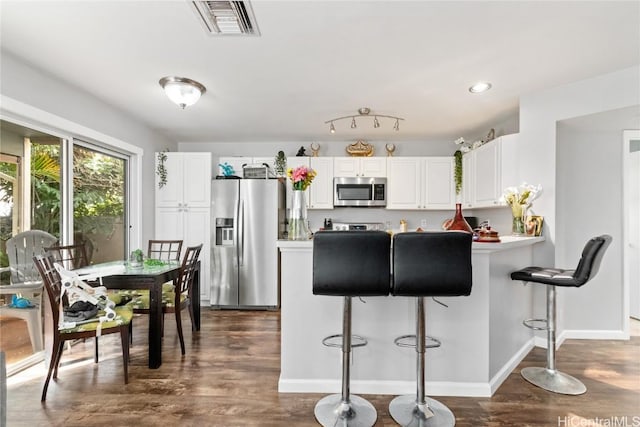 kitchen with dark hardwood / wood-style floors, a breakfast bar area, white cabinets, kitchen peninsula, and stainless steel appliances