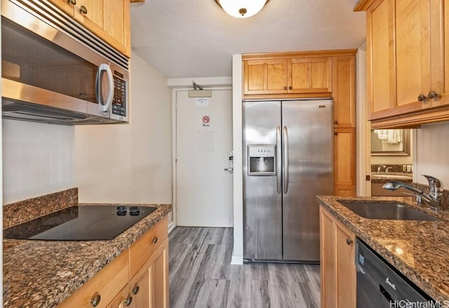 kitchen featuring dark stone countertops, sink, black appliances, and light wood-type flooring