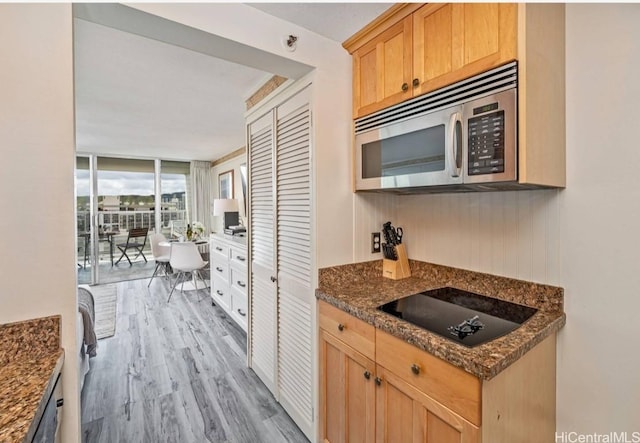 kitchen with black electric cooktop, floor to ceiling windows, dark stone counters, and light wood-type flooring