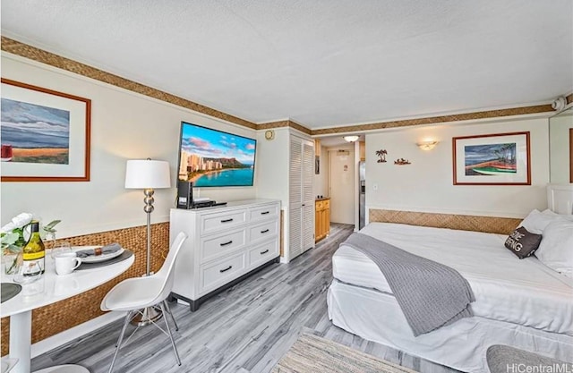 bedroom with ornamental molding, light hardwood / wood-style flooring, and a textured ceiling