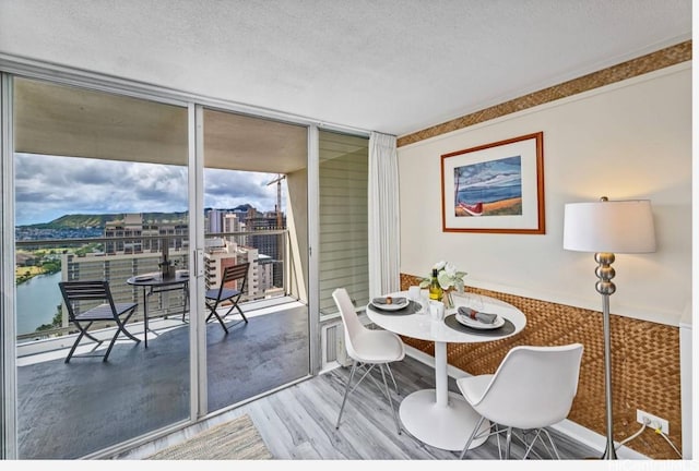 dining room featuring hardwood / wood-style flooring, a water view, a textured ceiling, and a wall of windows