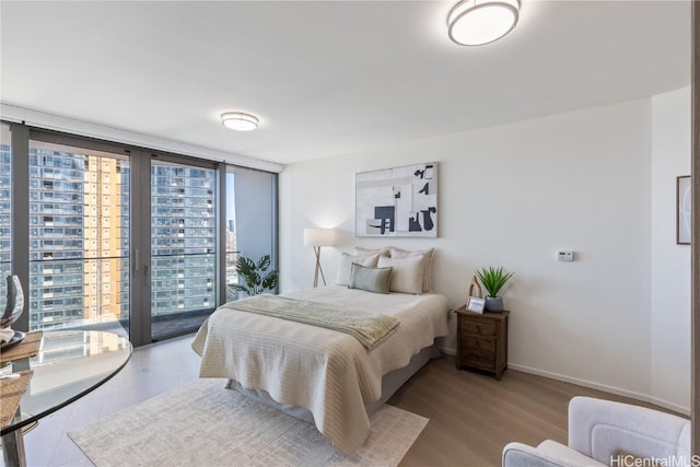 bedroom with a city view, baseboards, access to outside, light wood-type flooring, and floor to ceiling windows