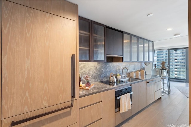 1000 Auahi St Unit 2505, Honolulu, HI 96814 - kitchen featuring black electric stovetop, glass insert cabinets, stainless steel oven, light wood-type flooring, and dark stone counters