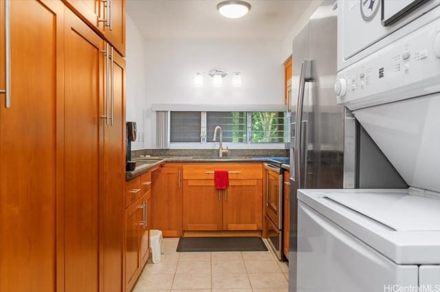 kitchen with sink, light tile patterned floors, stainless steel range with electric cooktop, and stacked washer and clothes dryer