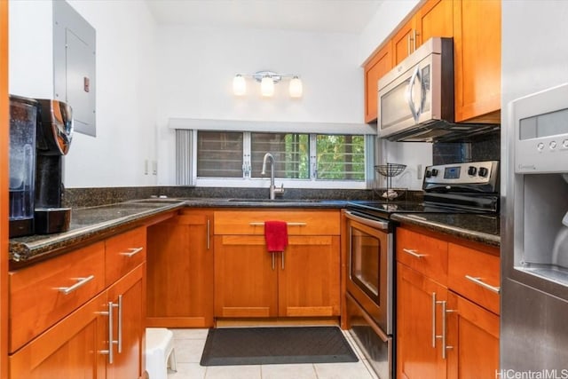 kitchen with appliances with stainless steel finishes, sink, dark stone counters, light tile patterned floors, and electric panel