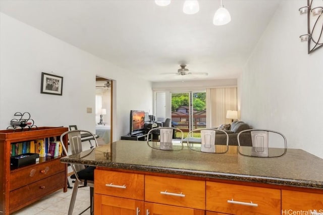 kitchen with a breakfast bar, pendant lighting, dark stone counters, light tile patterned floors, and ceiling fan